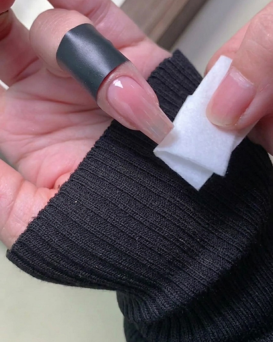 A lint-free wipe being used to clean the skin around the nail edges, removing excess iridescent powder.