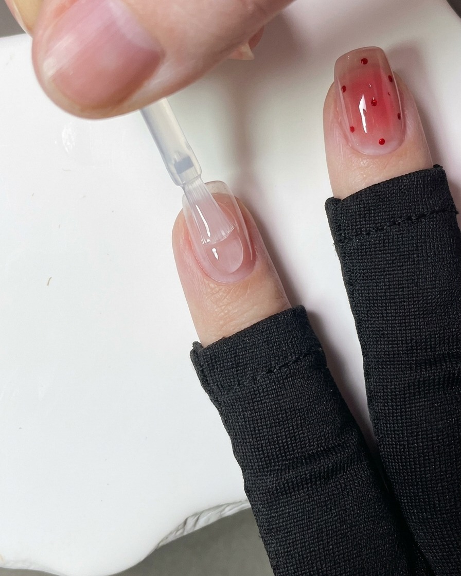 A close-up of a dotting tool applying small red gel dots onto a nail surface.