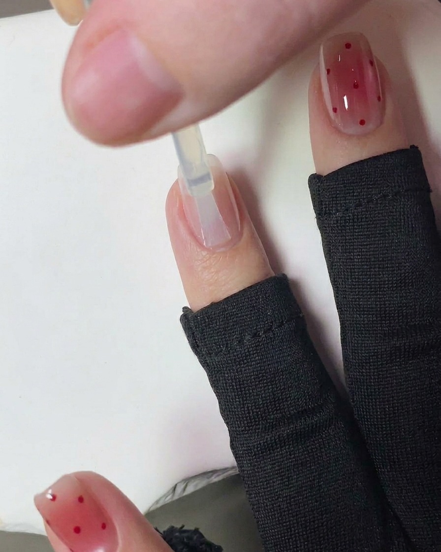 A hand with fresh red-dotted nails curing inside a UV nail lamp.