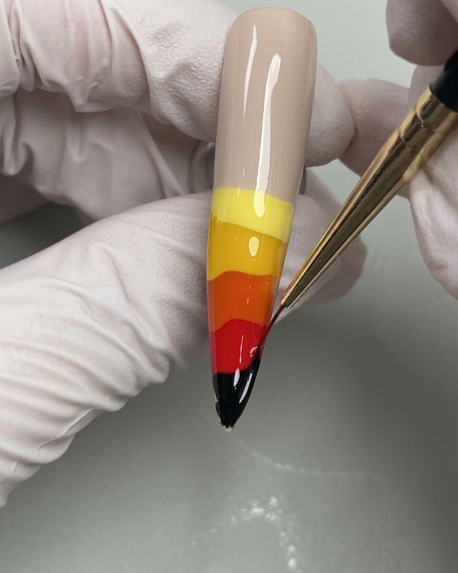 A fine liner brush dragging wet gel colors upwards to create flames.