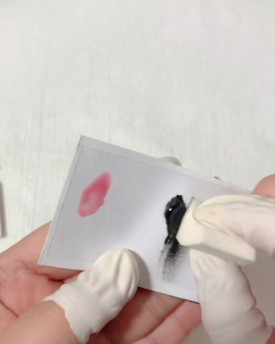 A close-up view of a hand wearing a finger cot dabbing a triangular sponge into black gel on a white palette.