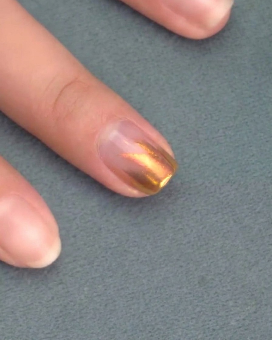 A brush applying a second layer of pink gel polish over the previous coat.