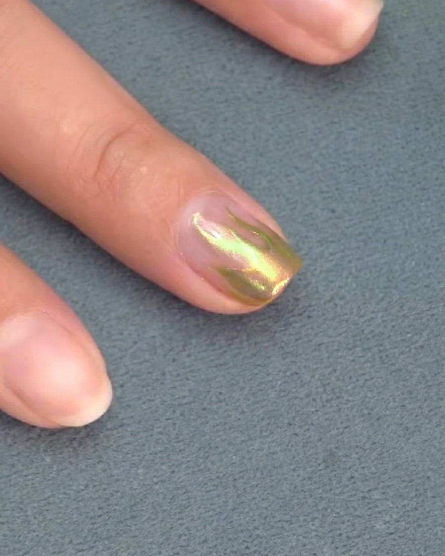A close-up of a liner brush perfecting the sharp tip of a flame design on a nail.