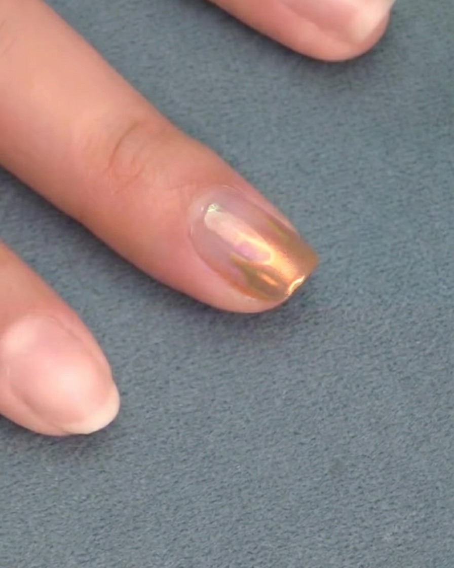 A brush applying a final clear top coat over a chrome-detailed nail.