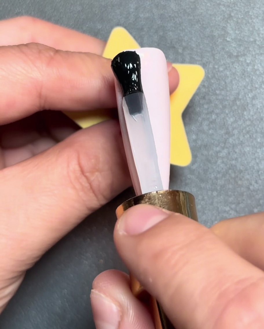 A brush applying a black line of gel polish horizontally across the tip of a pink nail.