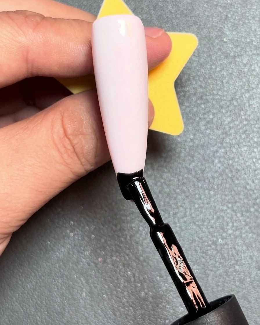 A brush applying a red line of gel polish just above the black line on a nail.