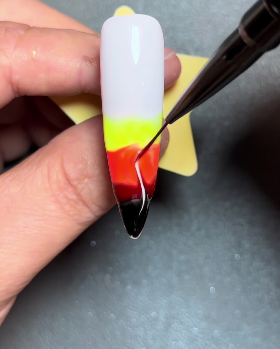 A close-up shot showing a liner brush dragging lines of color upward through the wet gel, creating flame shapes.