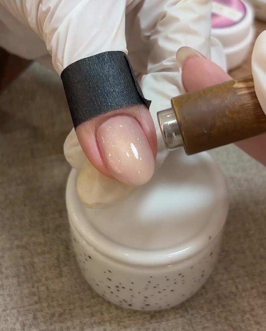 A close-up view of a magnet hovering over a nail coated in uncured cat eye gel, showing the magnetic particles shifting to create a bright line.