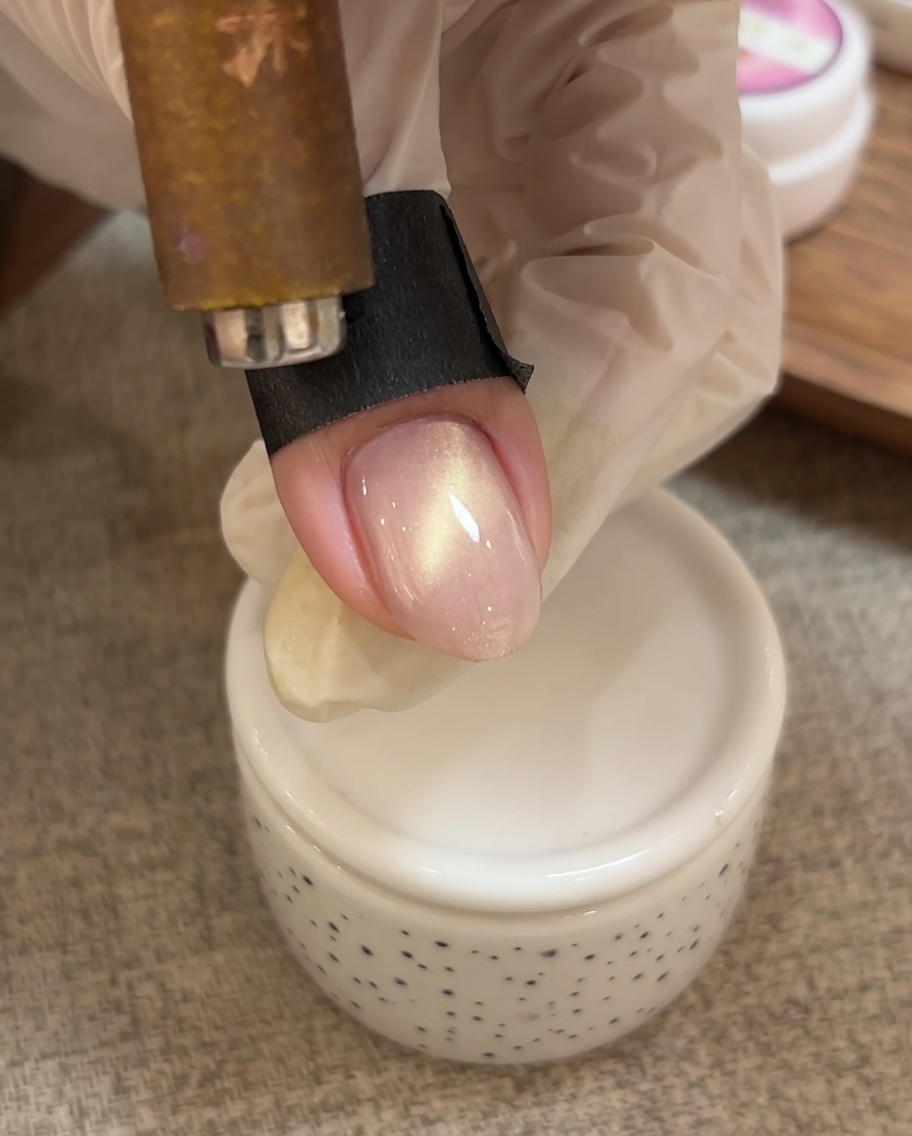 A hand using a magnetic tool to push the shimmering particles of the cat eye gel toward the tip of the nail.
