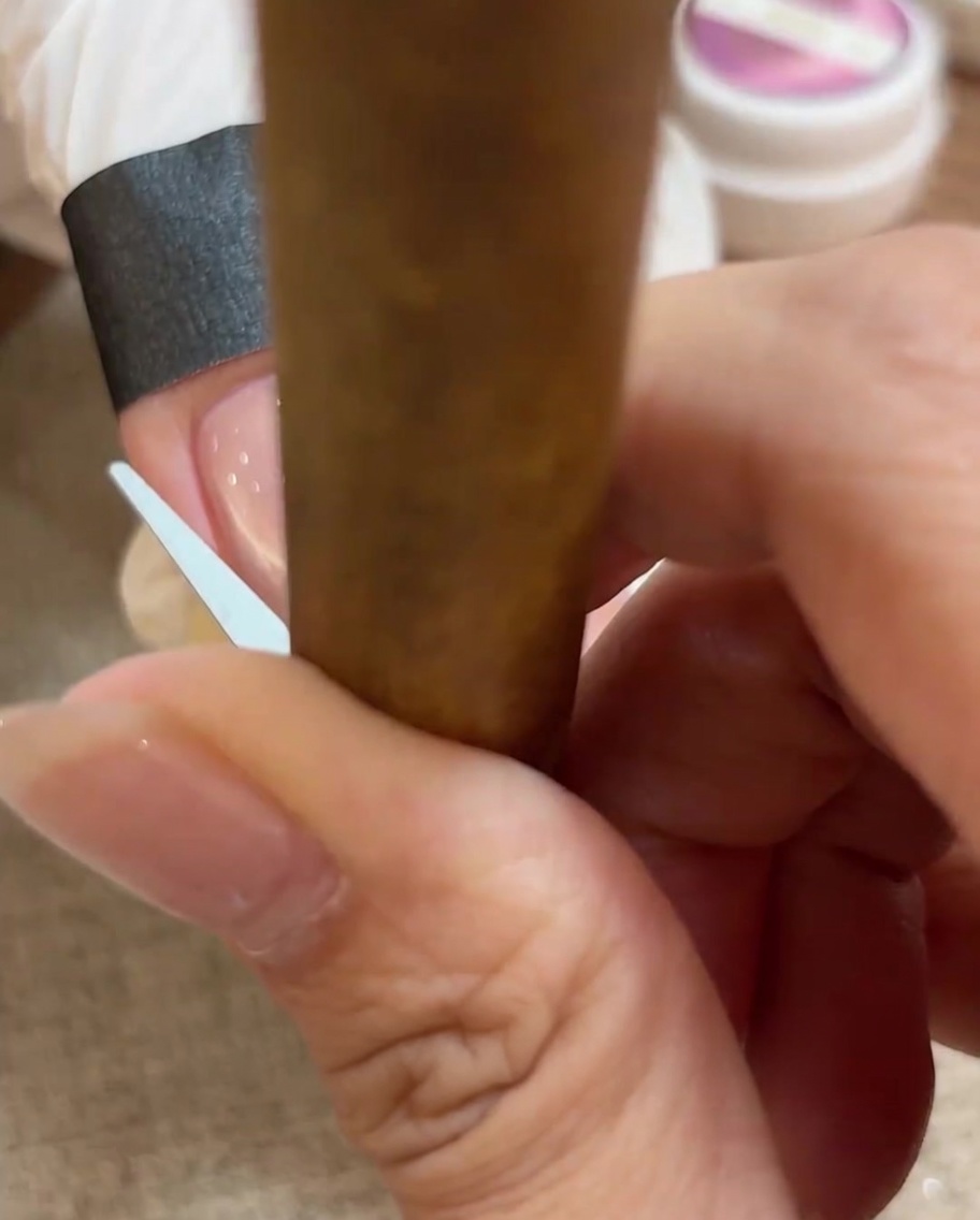 A close-up of a small tool being used to manipulate the cat eye gel into a perfect French-tip arc on the nail.