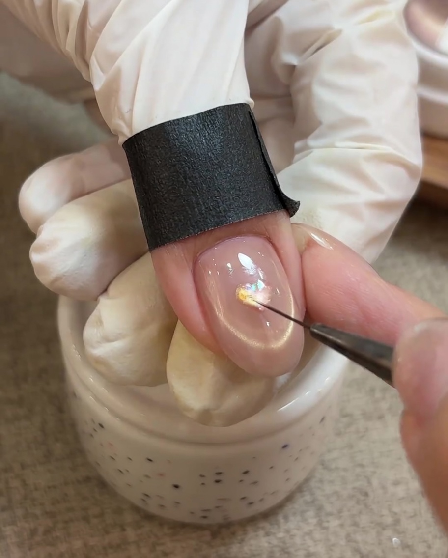 A detail tool placing a piece of opal foil onto the center of a pink heart nail design.