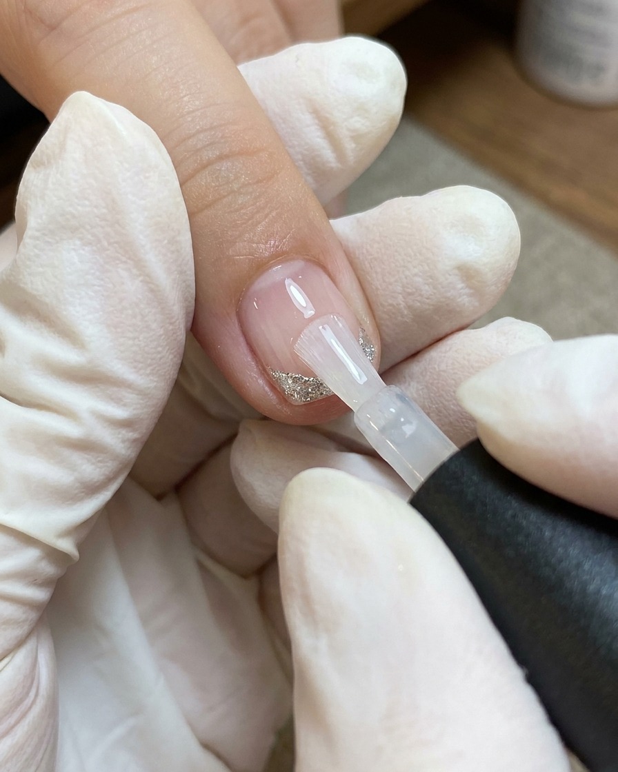 A brush applying a layer of clear top coat over a nail decorated with a heart and fine white and silver lines.