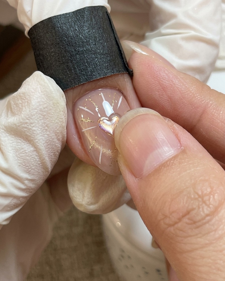 A close-up view of a nail art process where a thicker, clear gel is being carefully placed over a central heart motif.