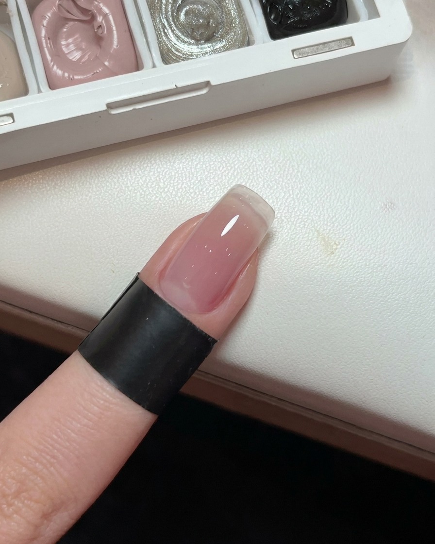 A close-up of a fingernail showing a smooth, light pink gradient gel base.