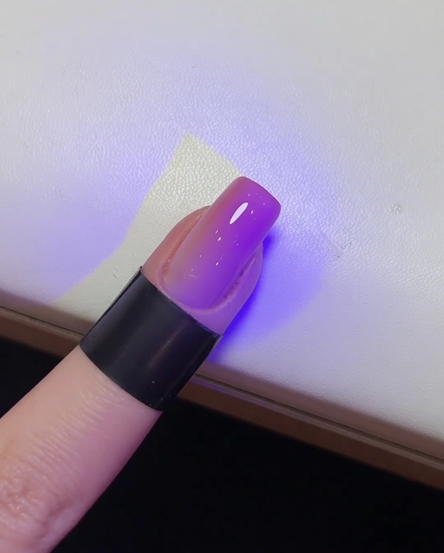 A close-up of a glossy, finished nail being cured under a UV lamp.
