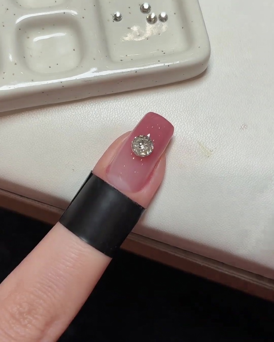 The main crystal set on a pink nail, positioned under UV lighting.