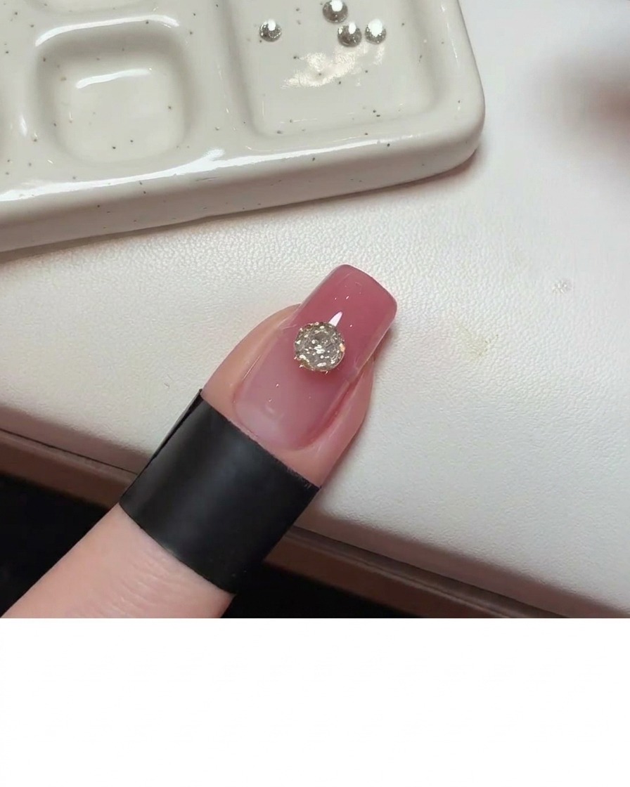 A precision tool applying clear adhesive gel to the nail surface directly beside the main crystal.