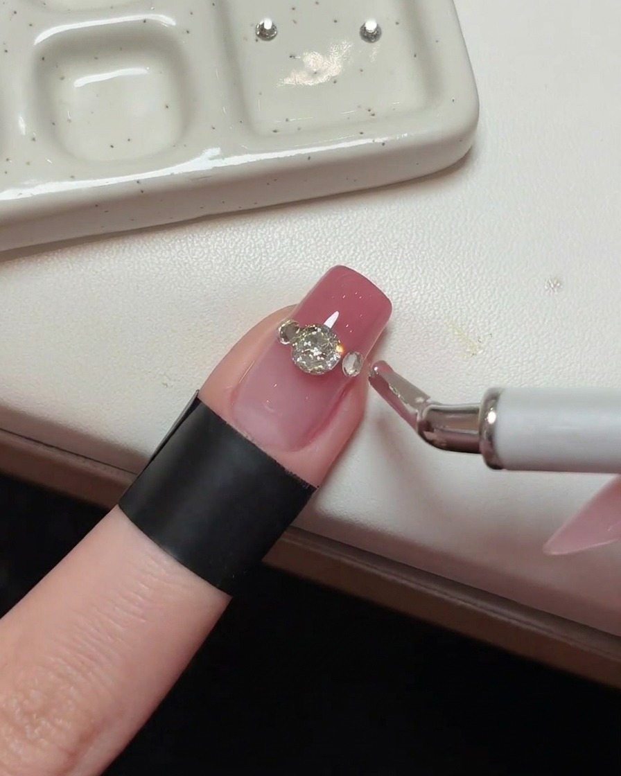 Close-up of a main crystal on a pink nail, with accent crystals being placed on the sides.