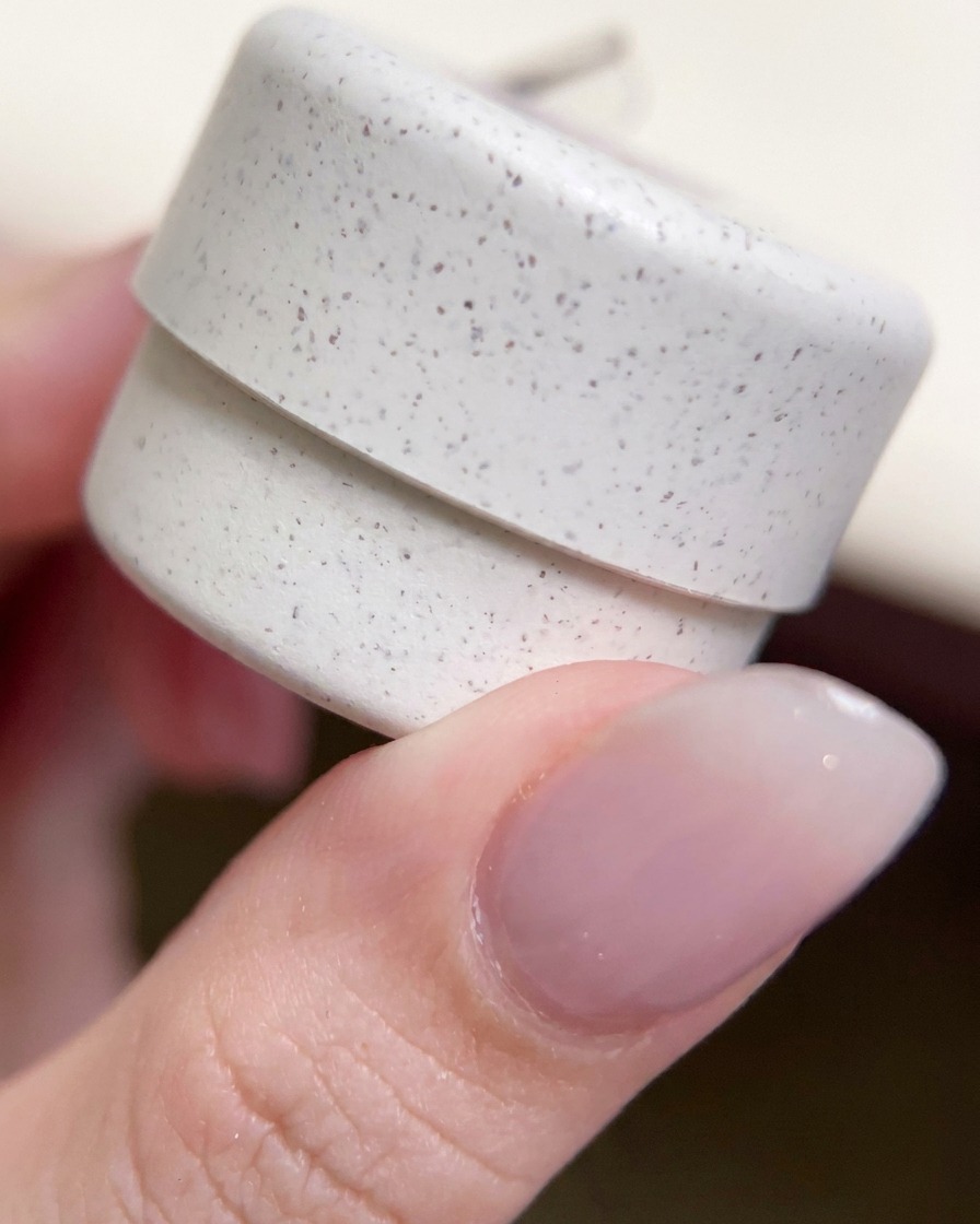 A close-up of a decorative, speckled gel polish jar held between fingers.