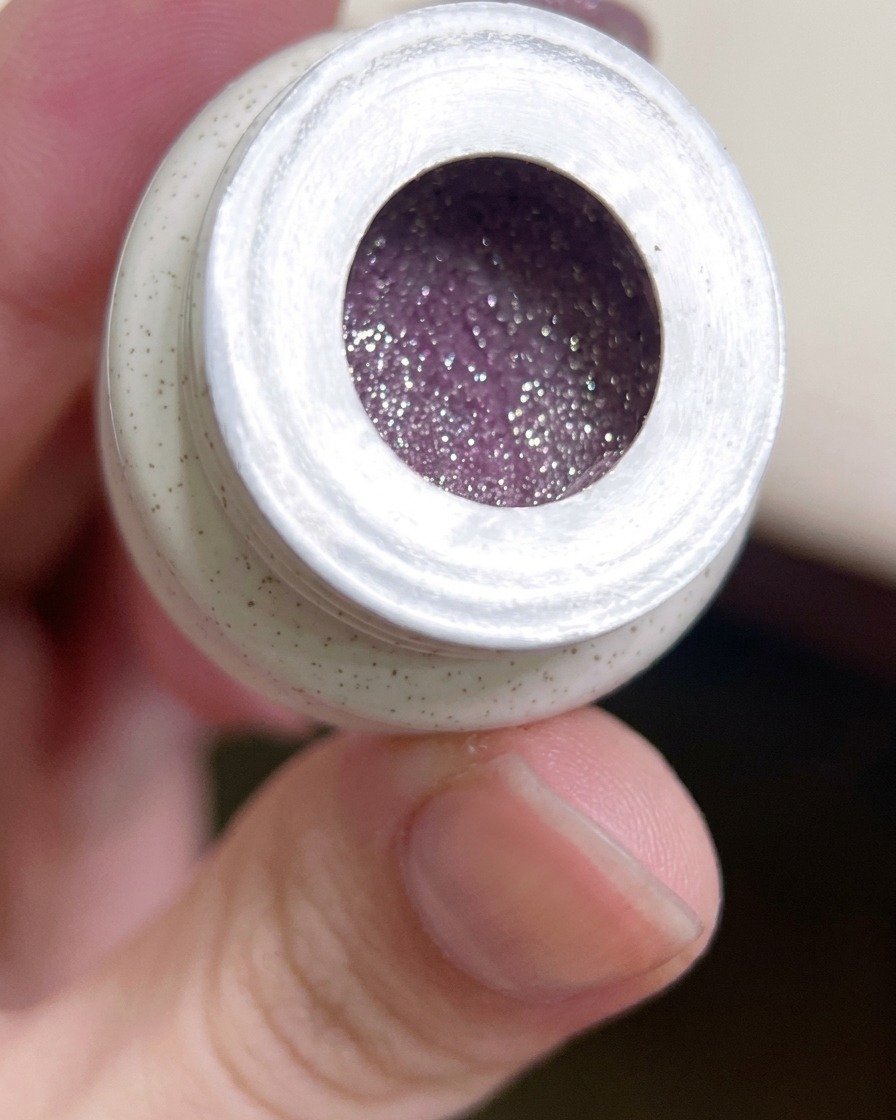 A flat gel brush dipping into a jar of vibrant, glittery purple gel polish.