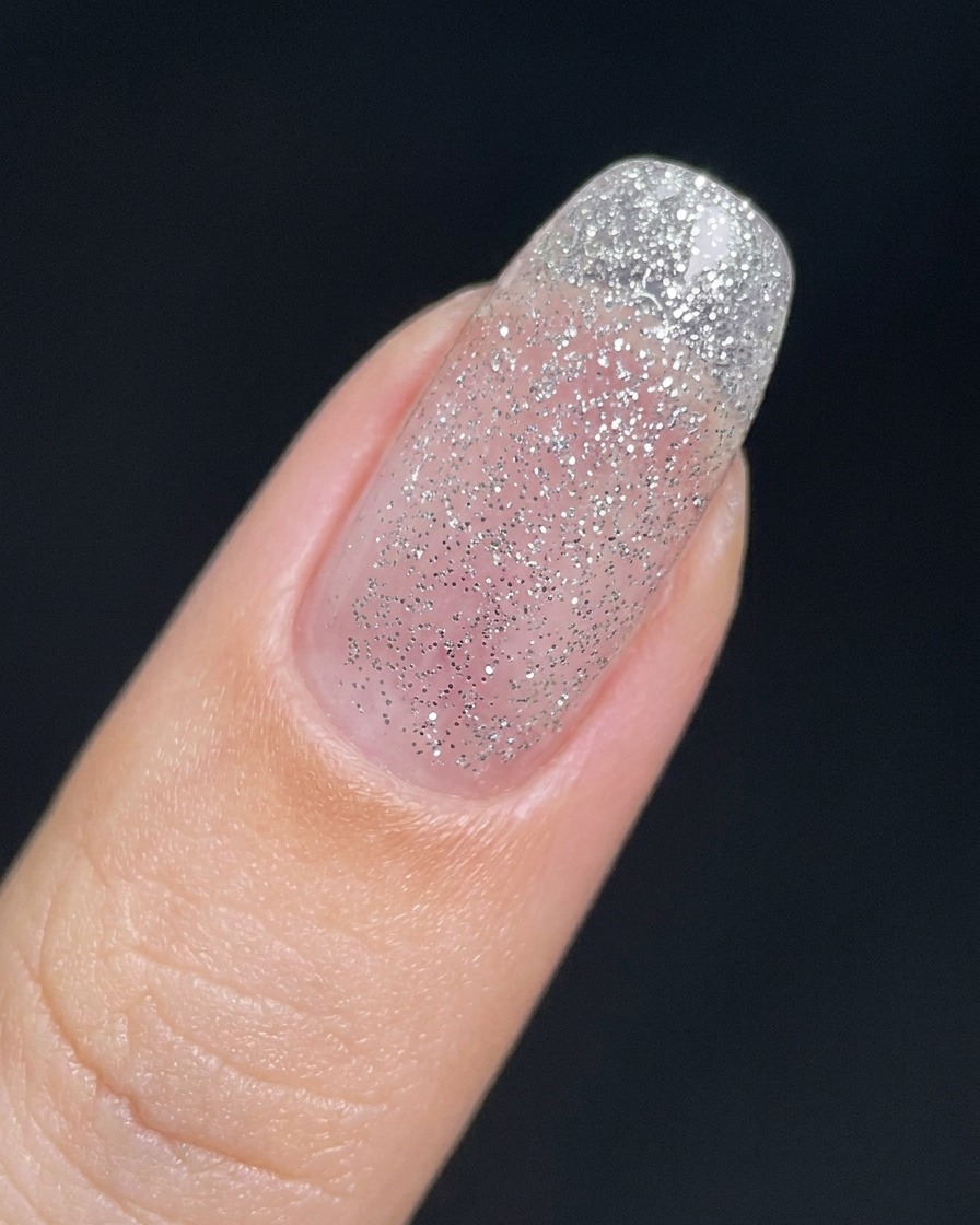 A fingernail covered in a thin, sheer layer of fine silver glitter gel.