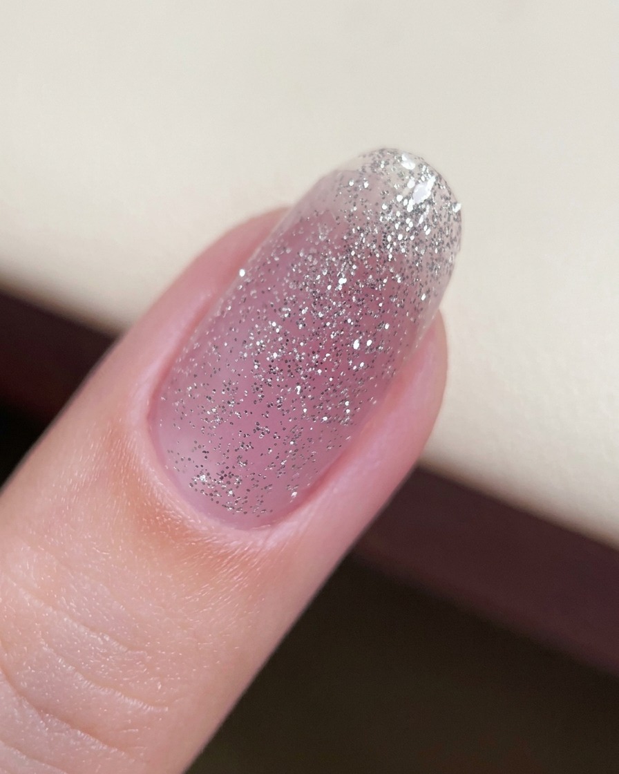 A close-up of a fingernail with a thin base layer of glitter gel applied.