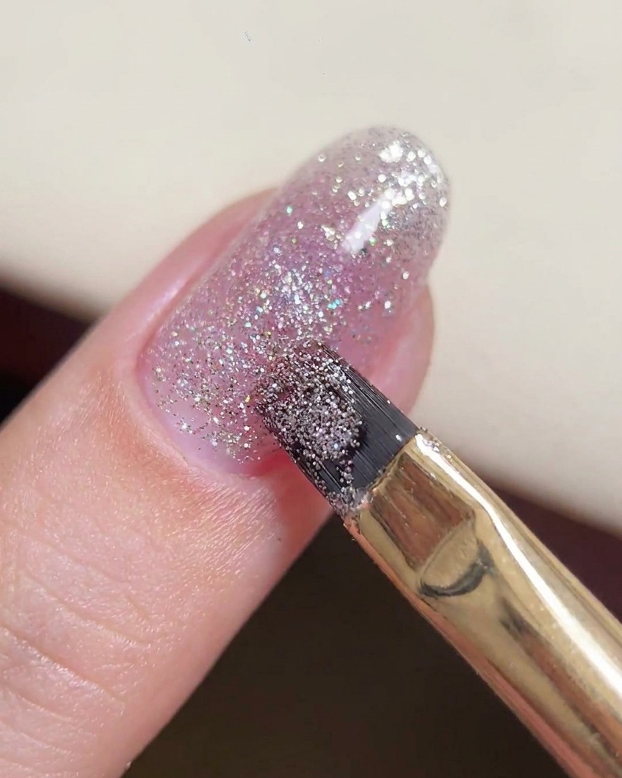 A gel brush manipulating a larger bead of glitter gel in the center of the nail.