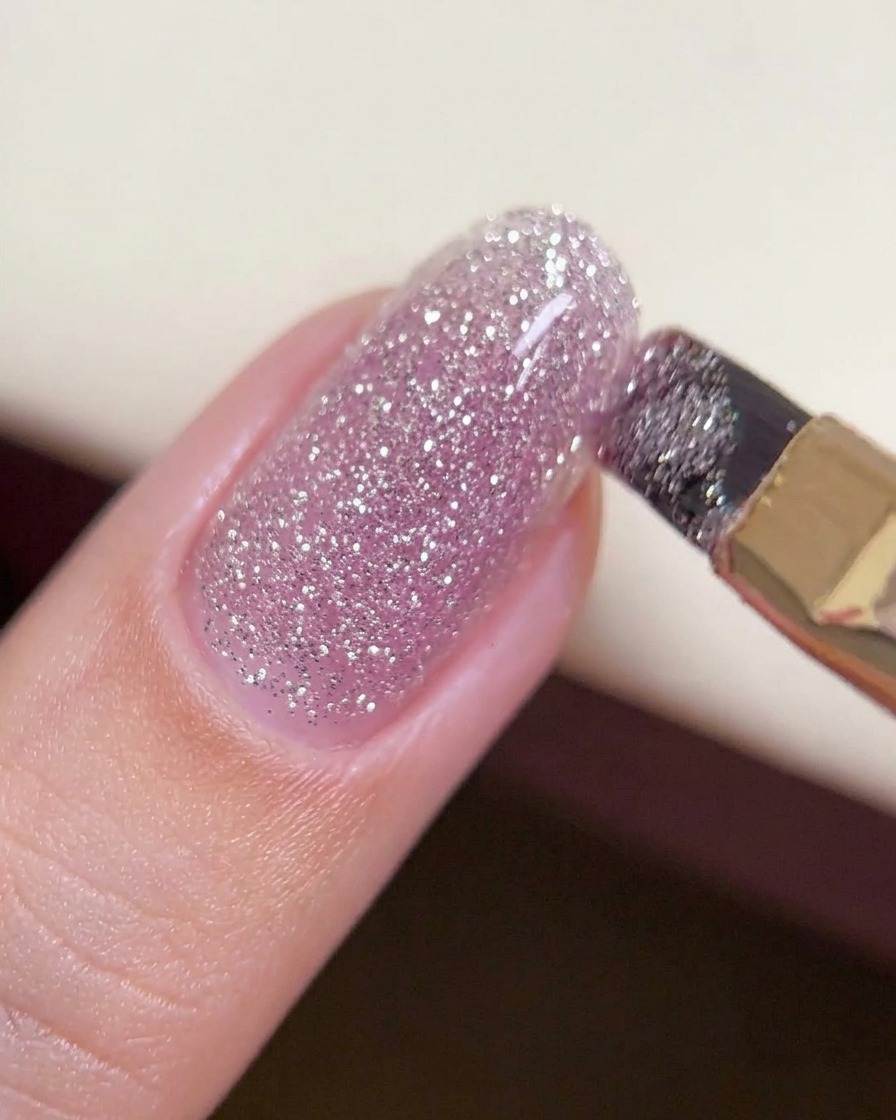 A brush gliding a thicker bead of crushed diamond gel across the center of a nail to create an even, structured layer.