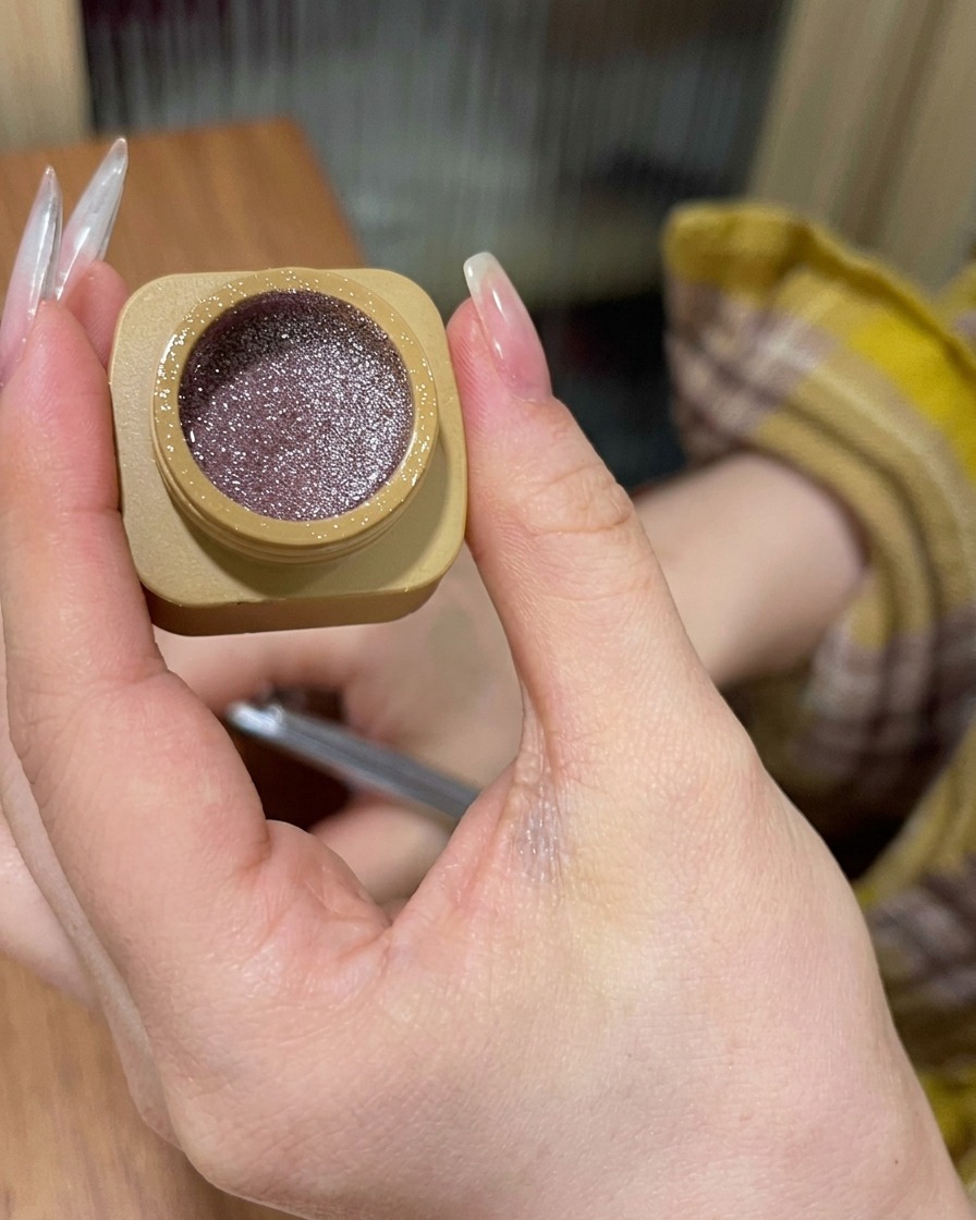 A close-up view showing pink glitter gel being applied to the nail base and blended downward.