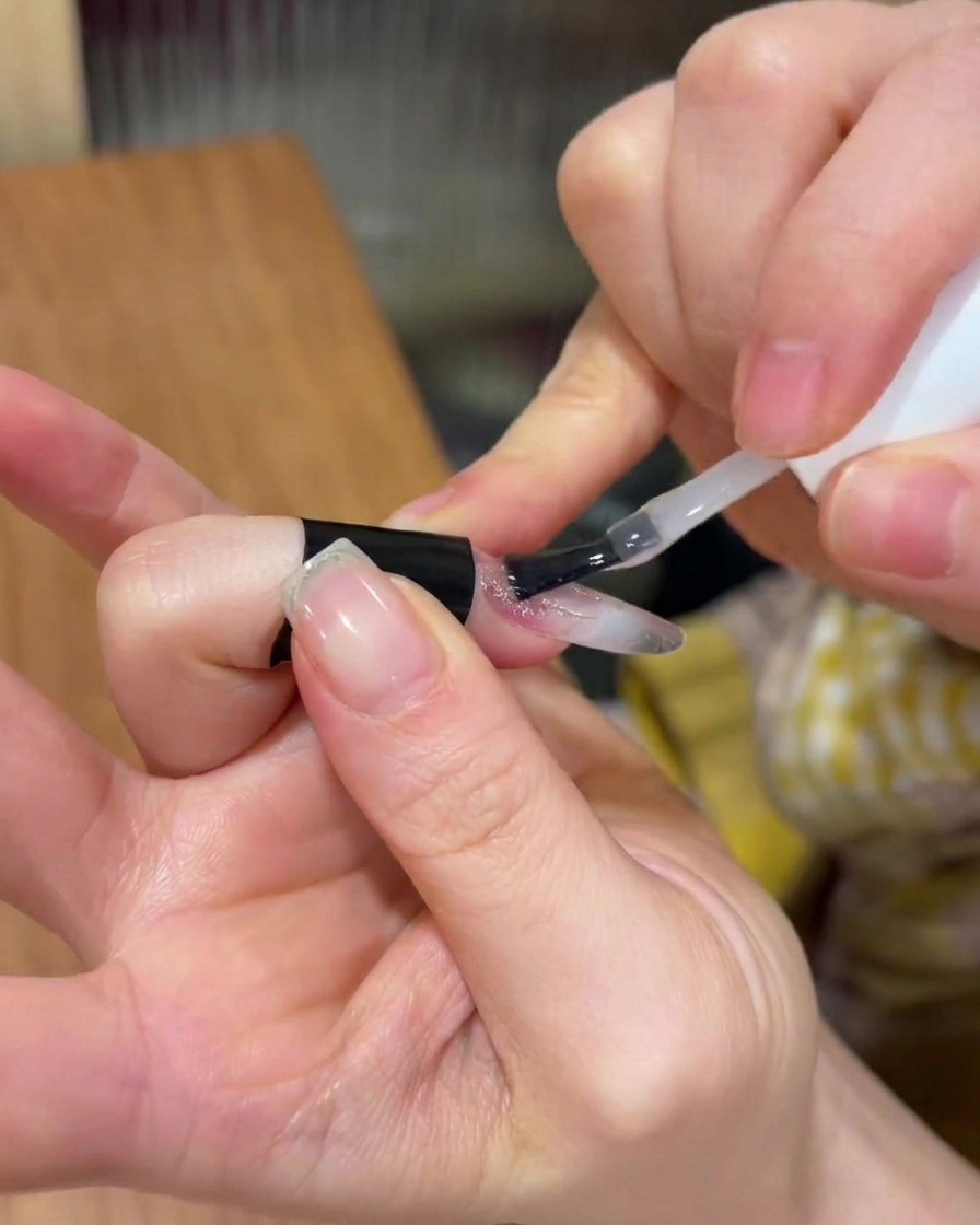 Applying a clear layer of builder gel over the existing nail design.