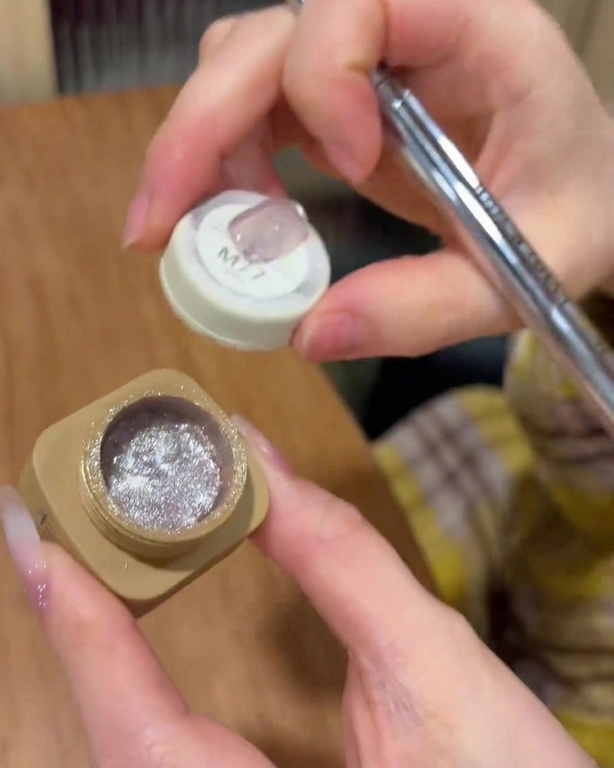 A brush applying cat-eye gel polish evenly over the nail surface.