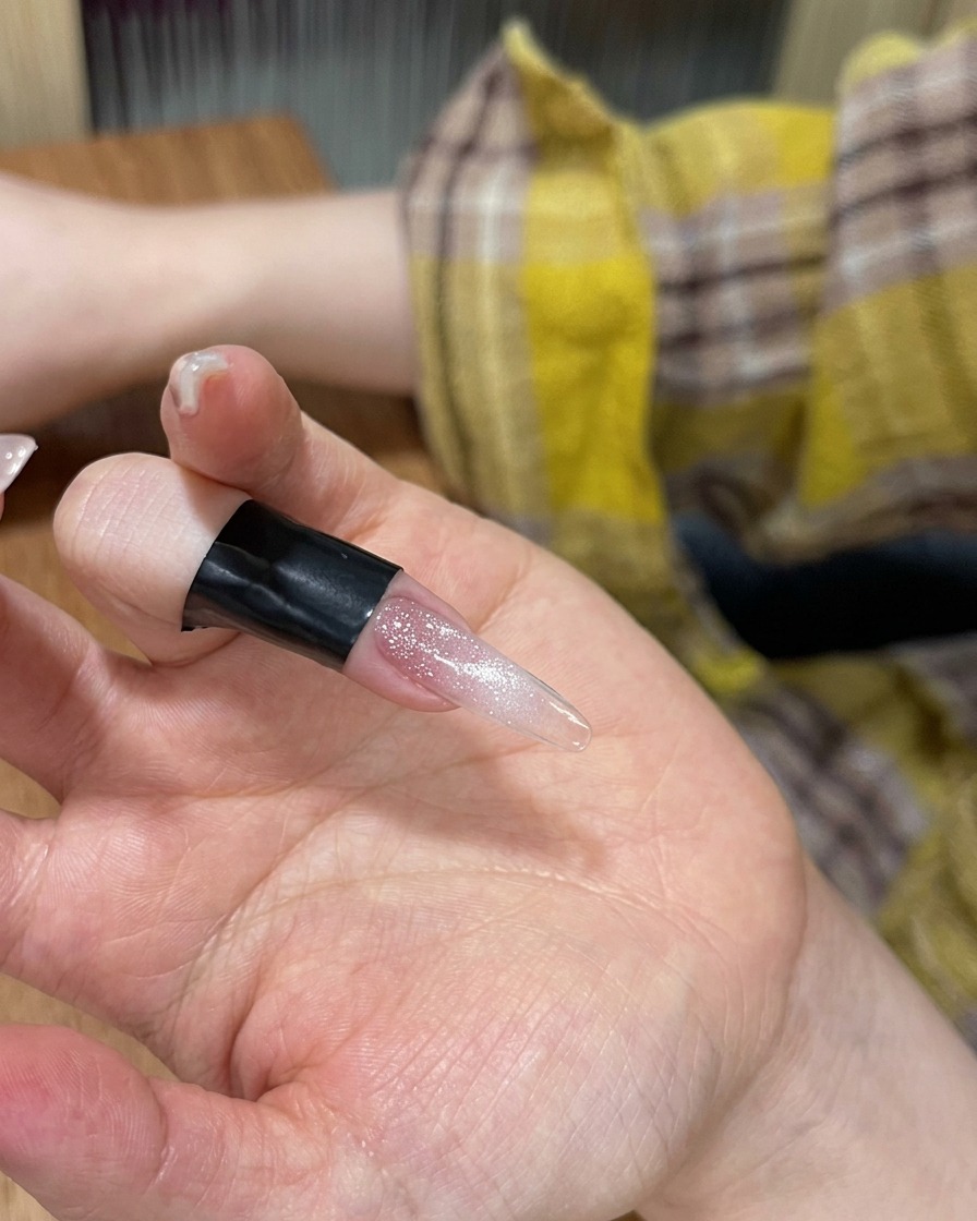 A close-up view of a finger with cat-eye gel polish resting inside a portable LED lamp.