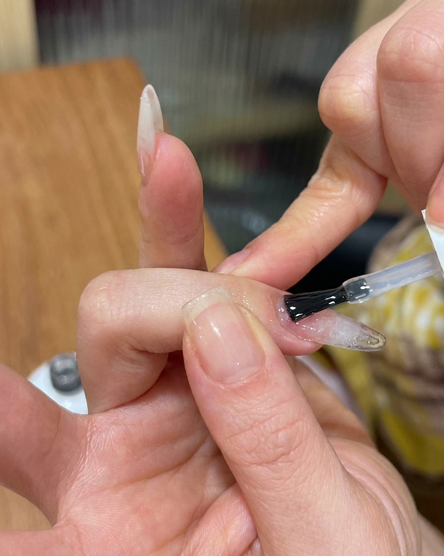 A brush applying a clear, glossy top coat over a textured, cat-eye gel nail.