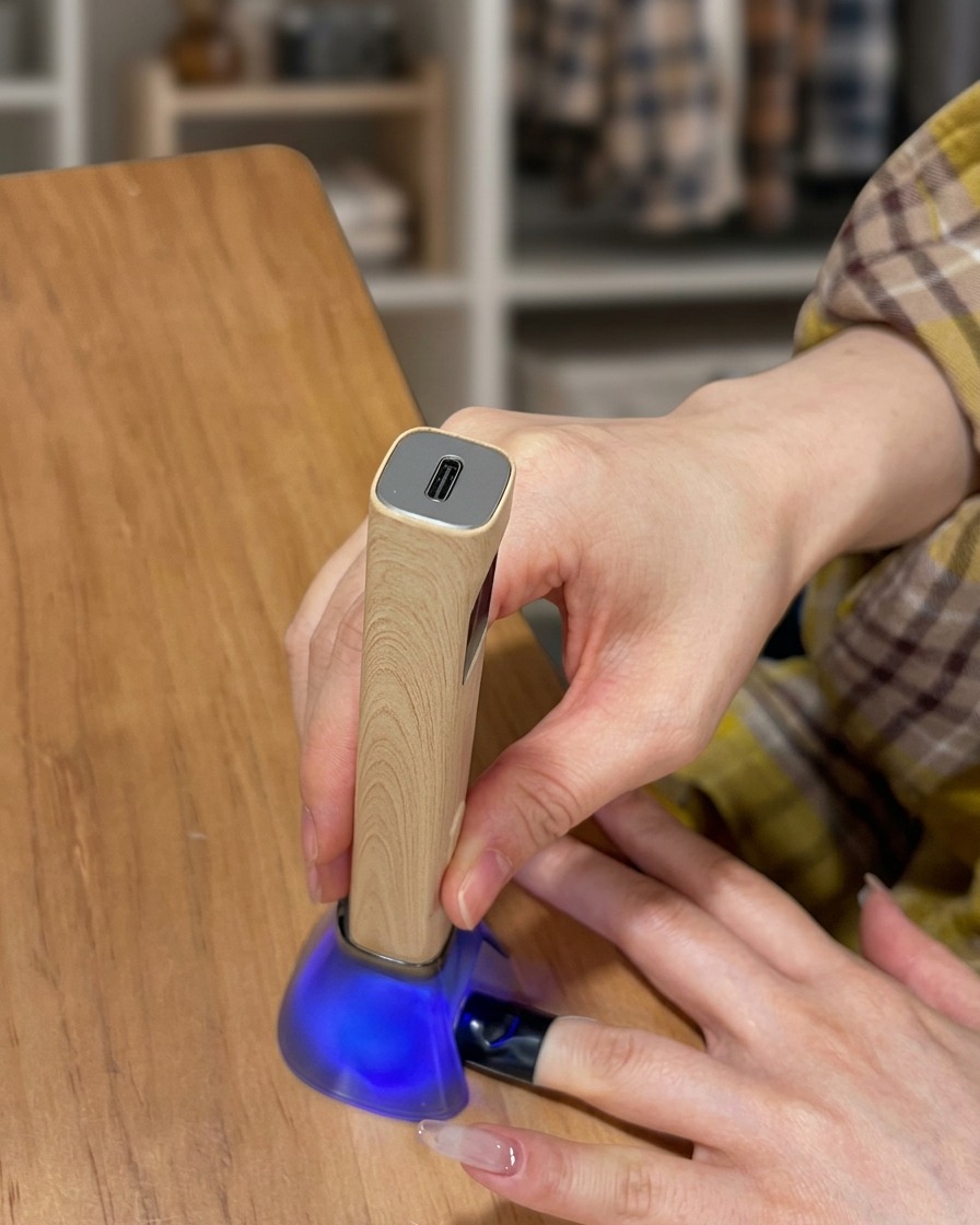 A finger resting inside a UV lamp while the top coat layer is curing.