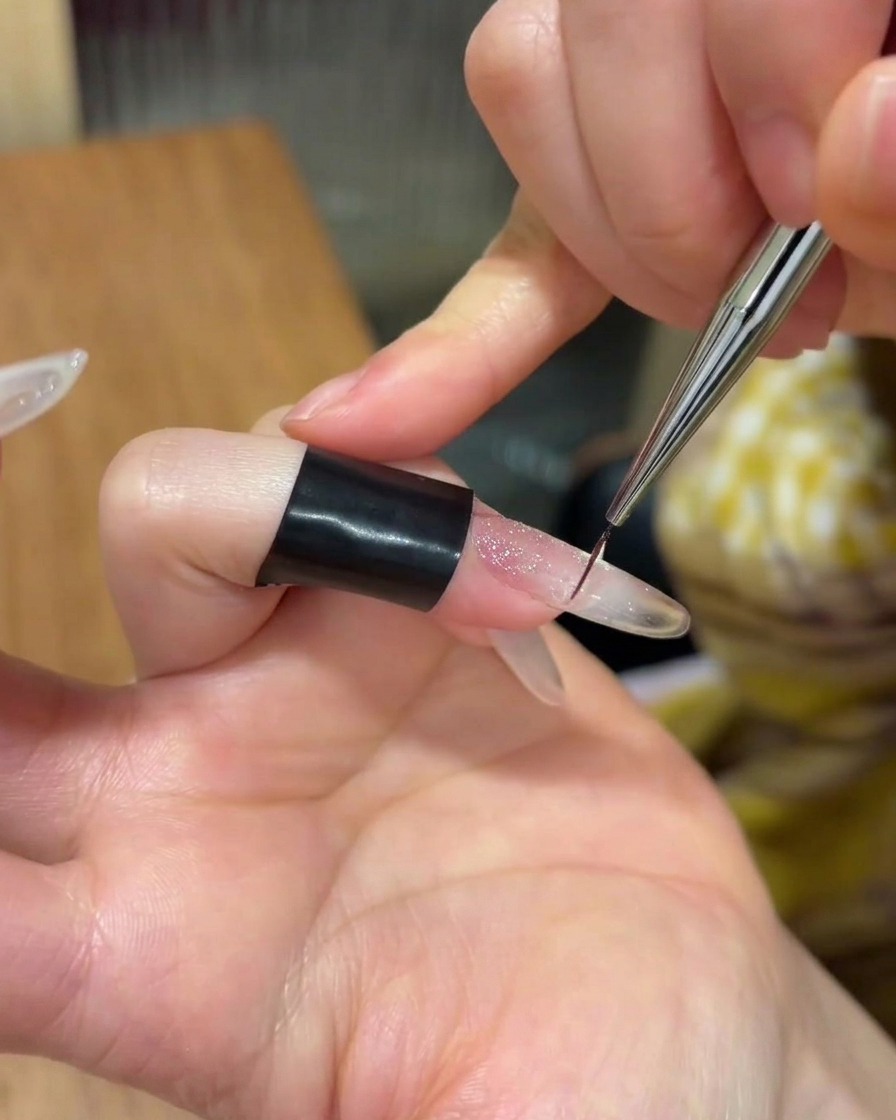 A small amount of clear adhesive gel being applied to the center of a manicured nail.