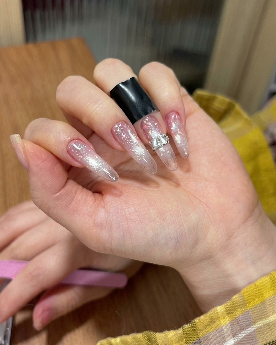 Tweezers carefully positioning a rectangular rhinestone onto a manicured nail.