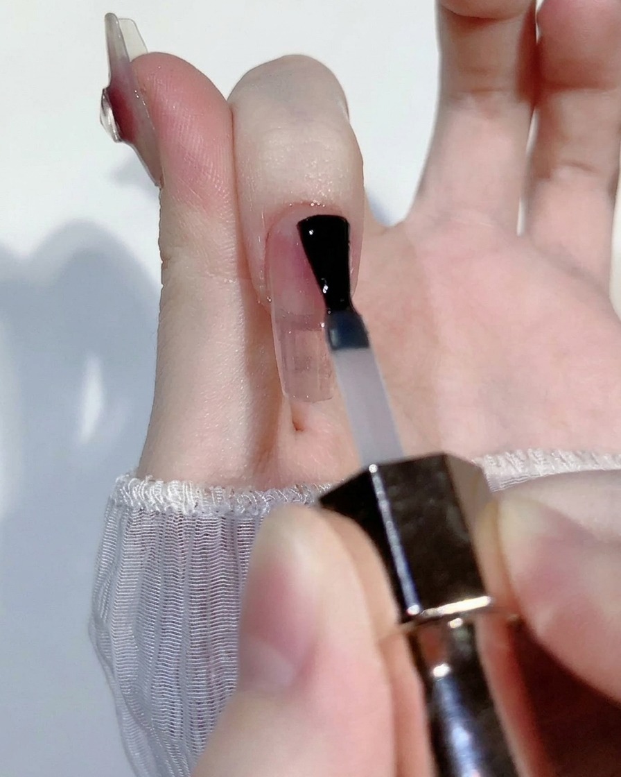 A small bead of sheer pink blush gel being applied to the center of a clear nail tip.
