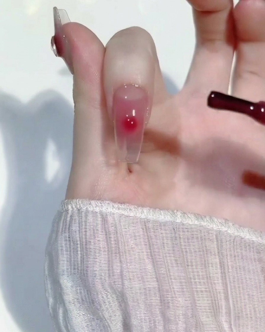 A small drop of pink gel being blended into the center of the nail using a detail brush.