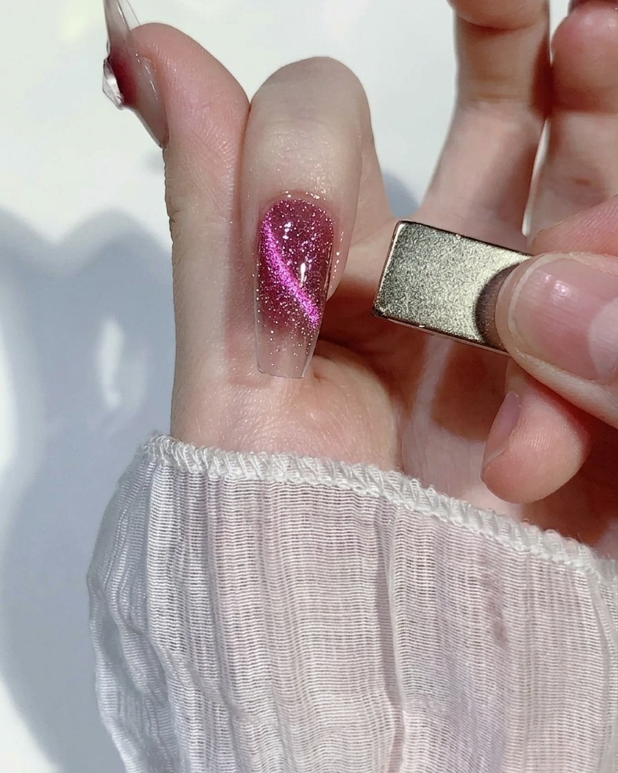 A rectangular nail magnet being held to the side of a pink glittery nail, pulling the magnetic particles into a focused line.