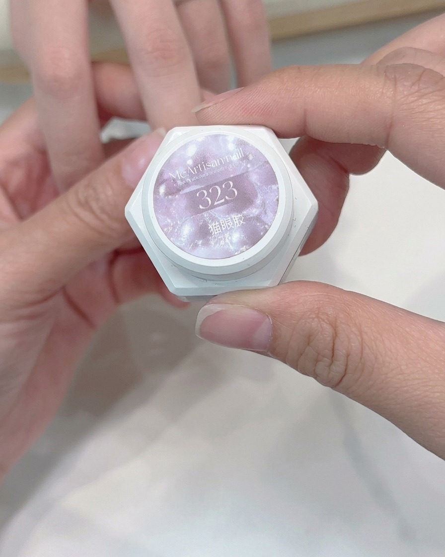A brush applying a layer of light-toned cat-eye gel to a nail.