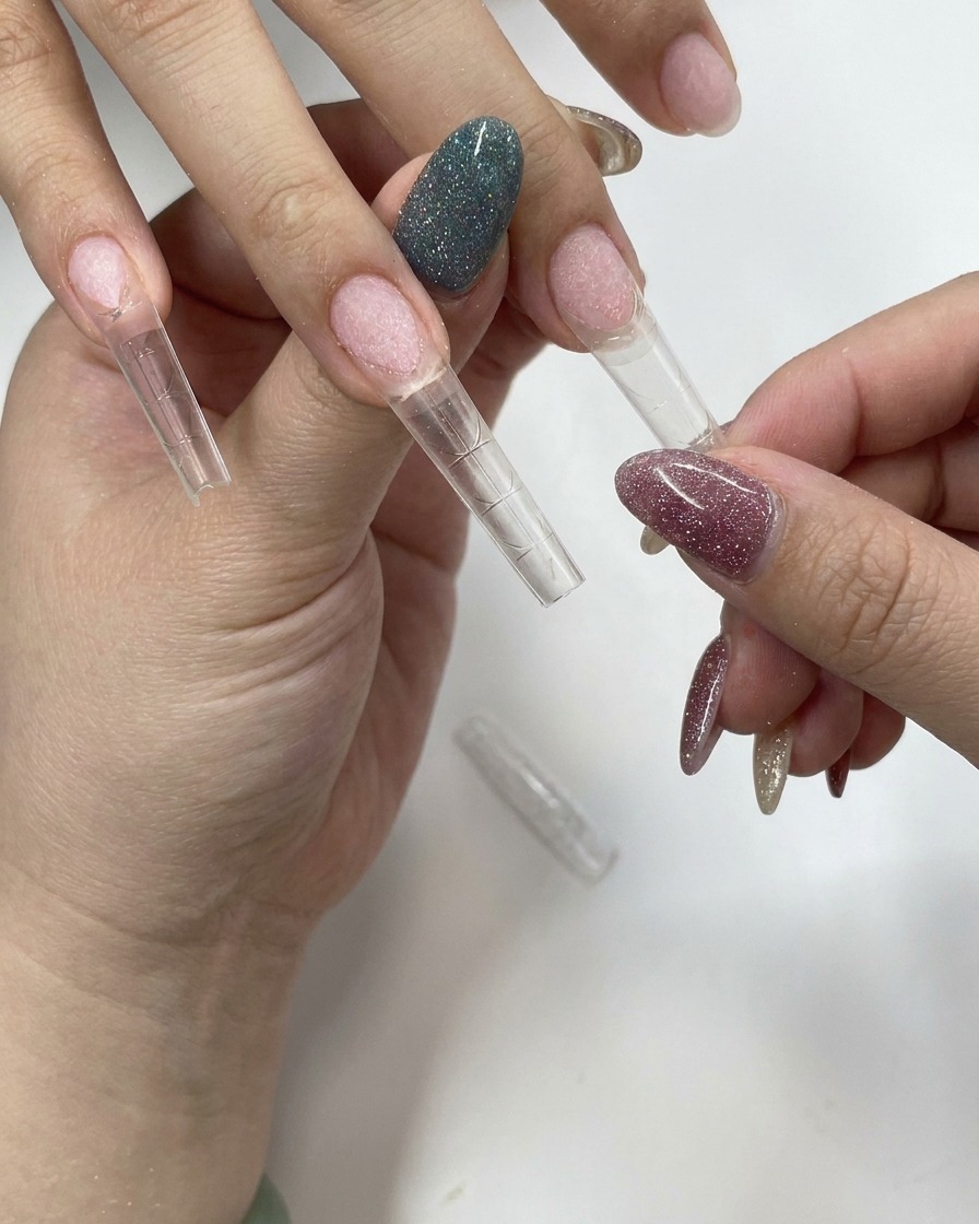 A hand firmly pressing a clear nail tip onto a natural fingernail.