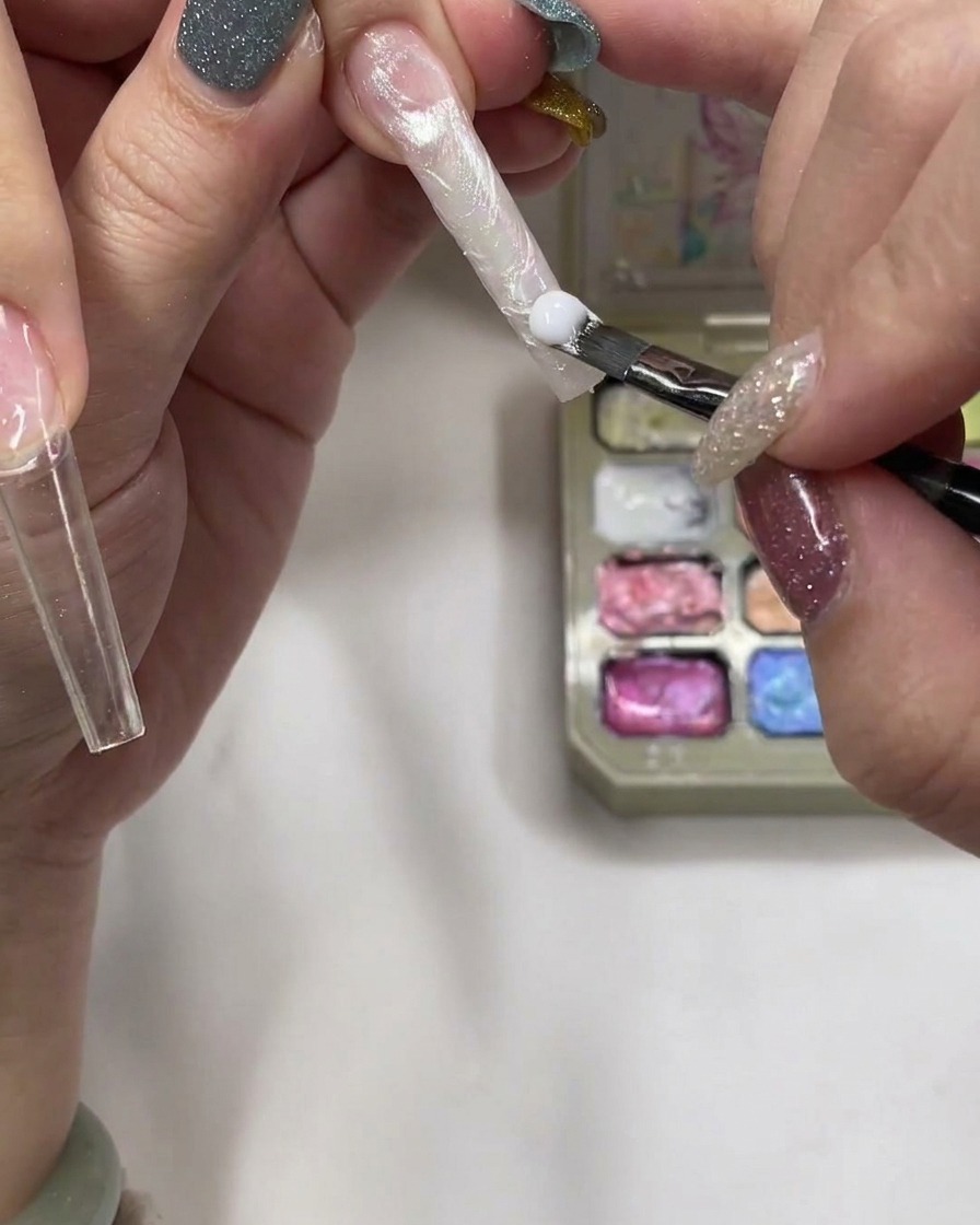 A brush applying a bead of thick, milky builder gel onto the nail bed.