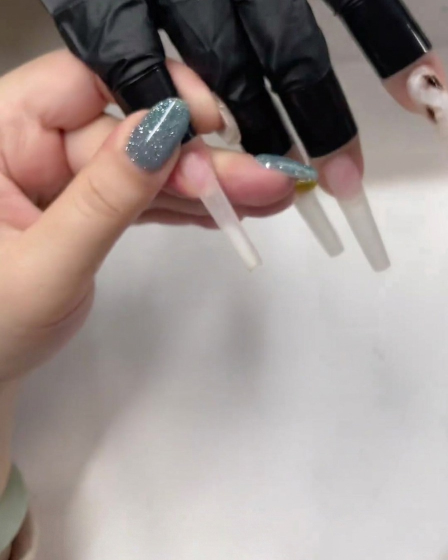 A detail shot of a brush applying a thin, clear layer of base gel onto a long, coffin-shaped nail.