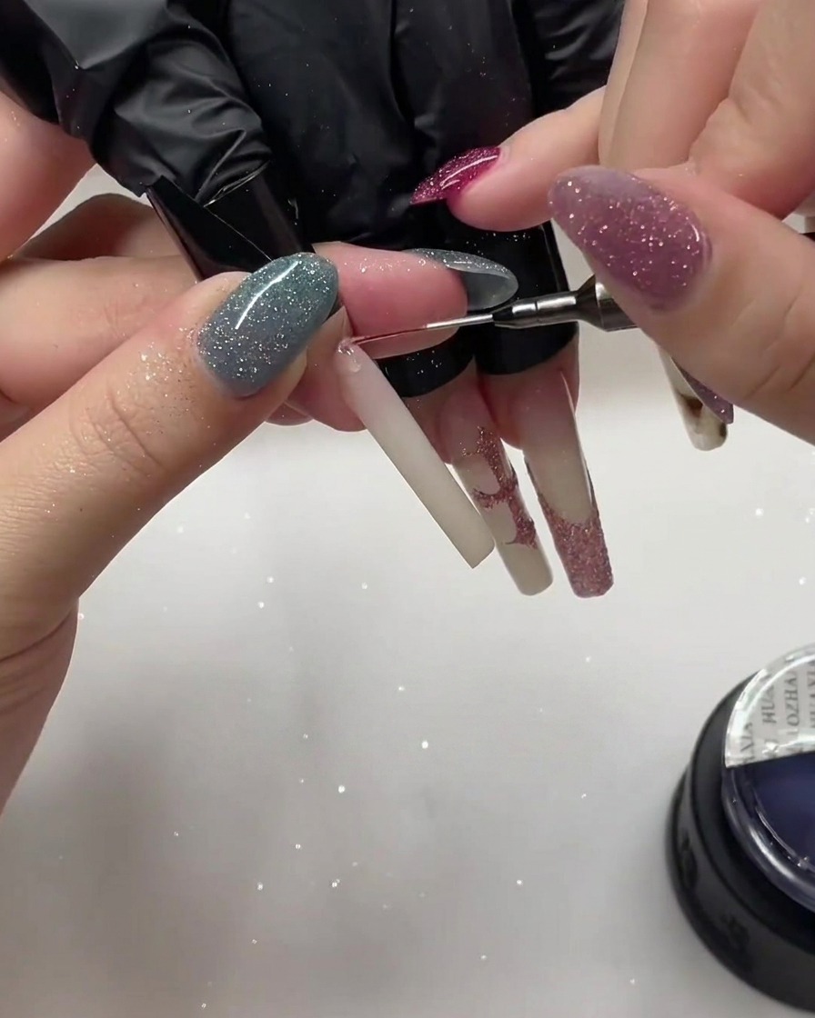 A close-up shot of a nail being layered with additional pink glitter powder using a detail brush.
