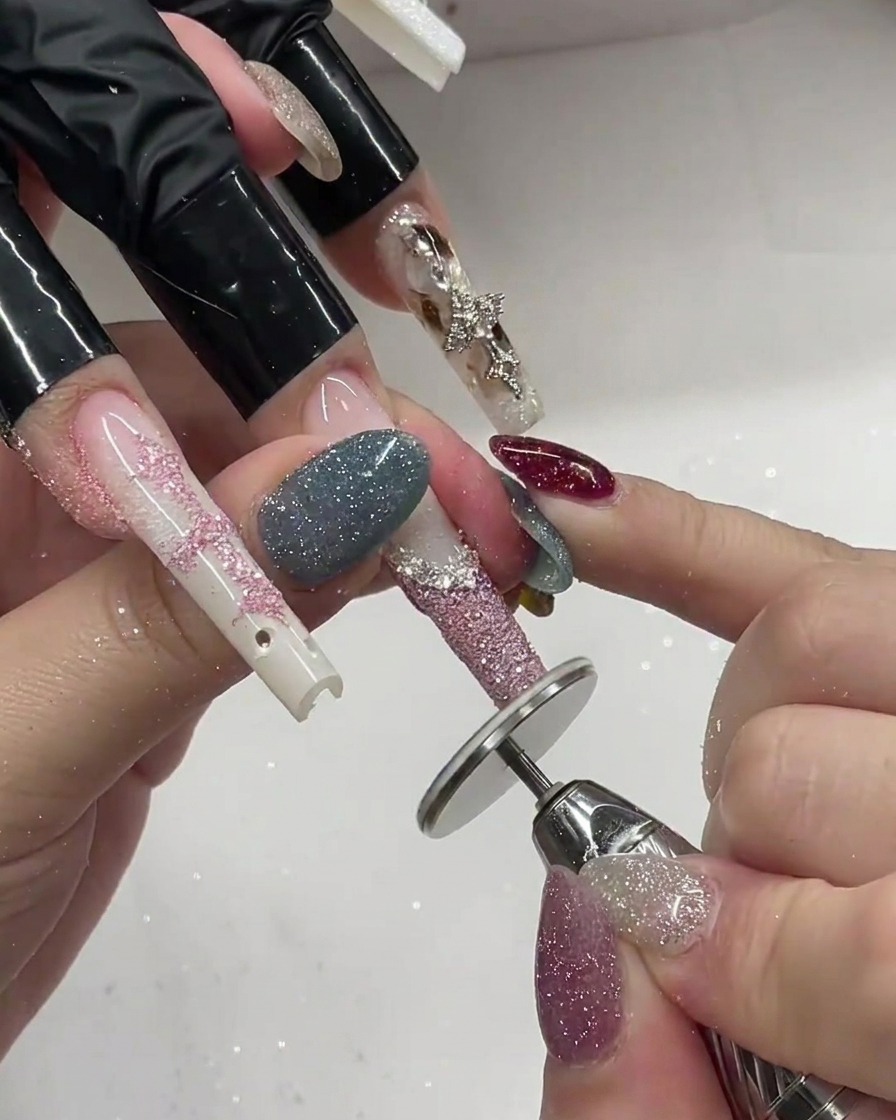 A brush applying fine pink glitter over a white gel French tip on a long nail extension.