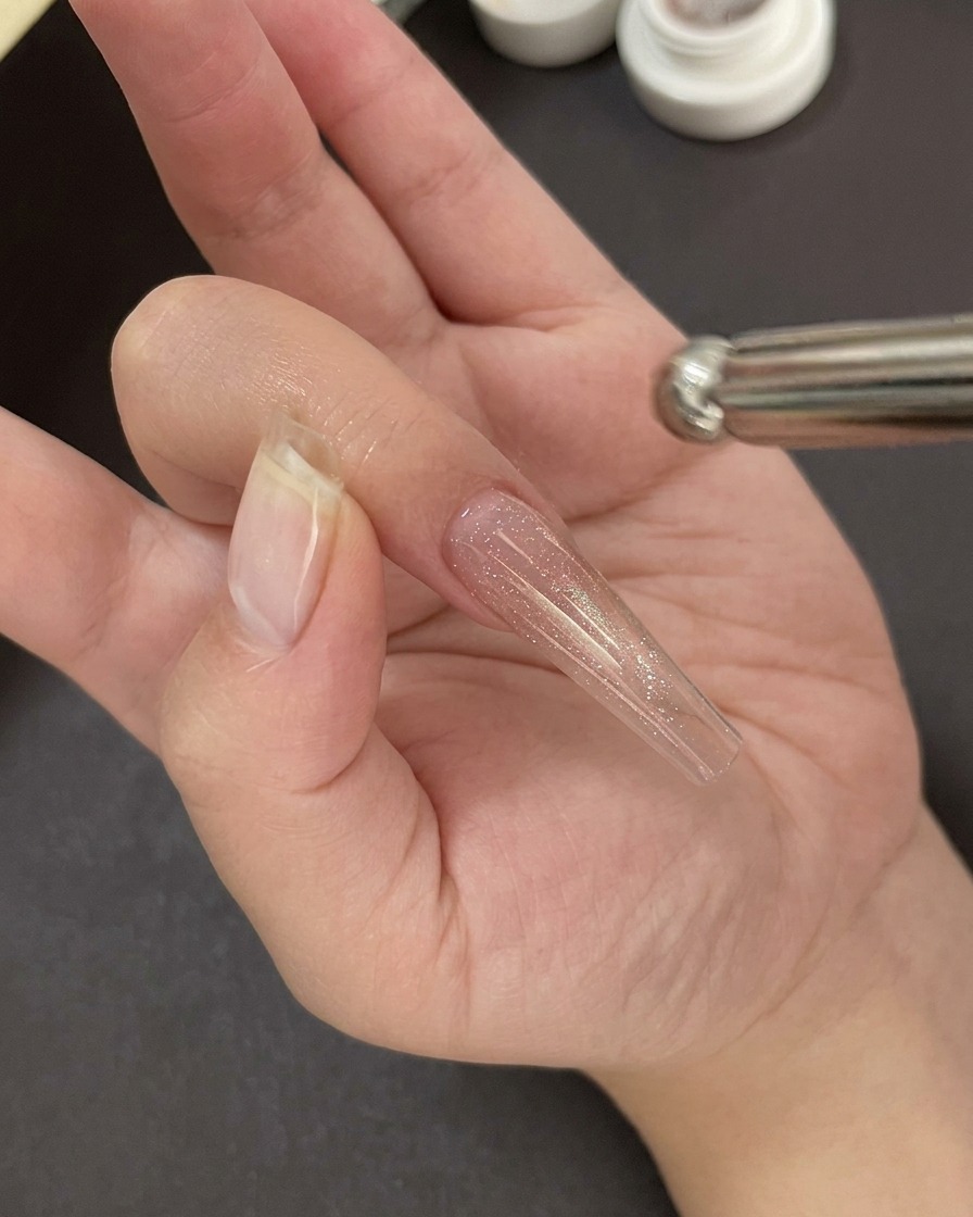 A hand positioned under a professional UV/LED nail lamp curing the gel base coat.