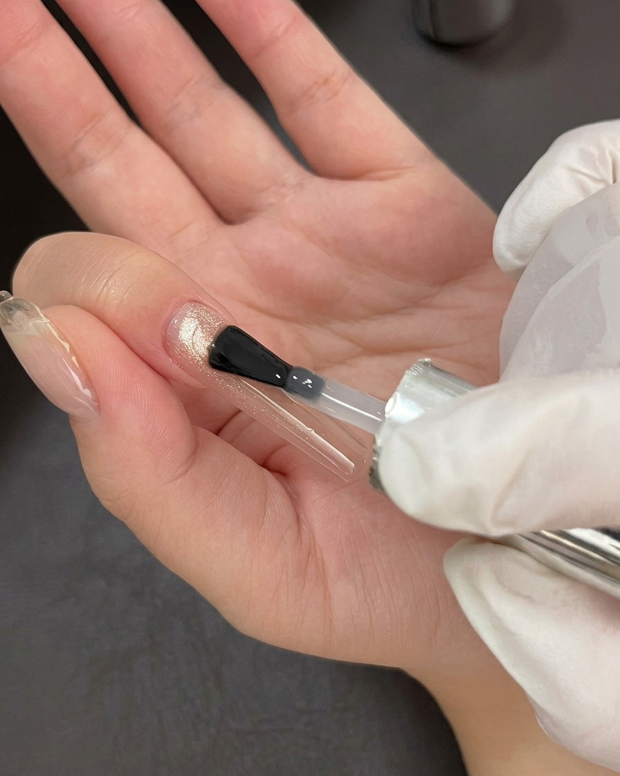 A professional nail brush applying a clear, glossy top coat over a shimmering cat-eye gel base.