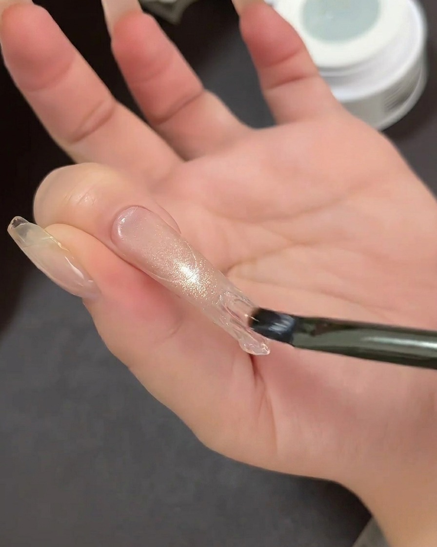 A close-up of a French tip guide sticker being placed on a nail extension to outline the tip area.