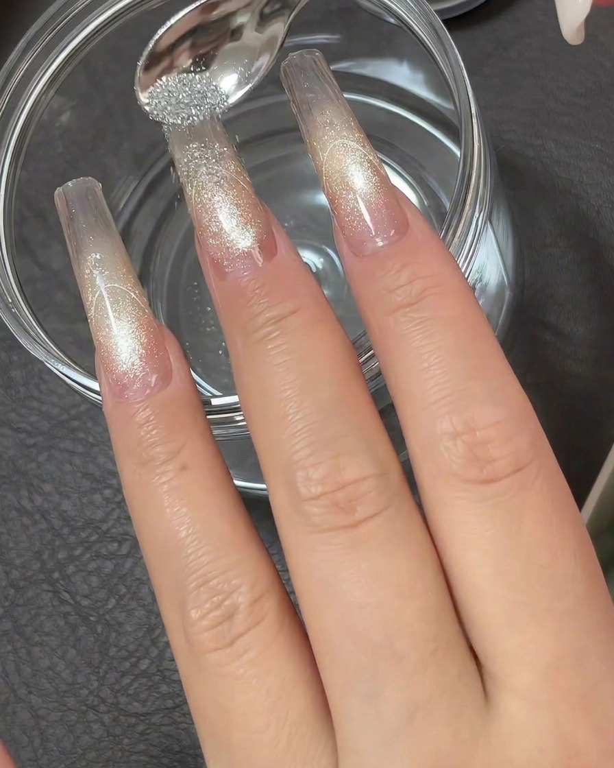 A small metal spoon showering highly reflective silver diamond powder over the sticky tip of a clear nail extension.