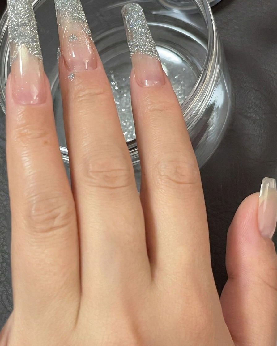 A close-up of a finger being gently tapped to shake off loose glitter powder from the nail tip.